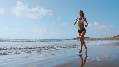 Fitness-runner-woman-running-on-beach-listening-to-music-motivation-with-phone-case-sport-armband-strap.-Sporty-athlete-training-cardio-barefoot-with-determination-under-summer-sun.